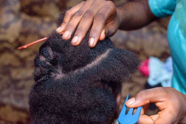 Hands of an african Nigerian hair dresser or stylist making weaving hairstyle for a client in saloon