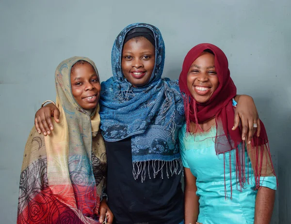 Three African Nigerian female muslim sisters or friends with Hijab scarves, standing curdled together with happy expression which is mostly seen during ramadan and other islamic festive seasons