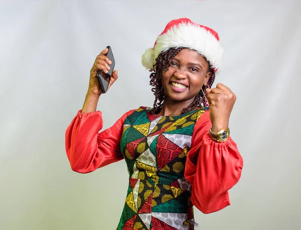 A joyful african lady from Nigeria holding a smart phone and also having a christmas cap on her head
