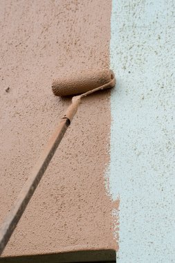 A long paint brush or roller painter of a mason painting and renovating the wall of a architectural building to make it more beautiful