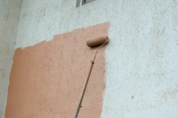 A long paint brush or roller painter of a mason painting and renovating the wall of a architectural building to make it more beautiful