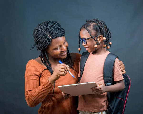 An african Nigerian mother, teacher or guardian helping a girl child with her studies with the help of a an education smart tablet