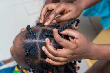 Hands of an african hair stylist or mother making braided hairstyle on the head of a little girl child at a saloon