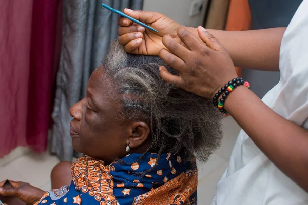 Hands of an hairdresser, stylist or entrepreneur making and weaving the grey hair of an elderly African Nigerian woman
