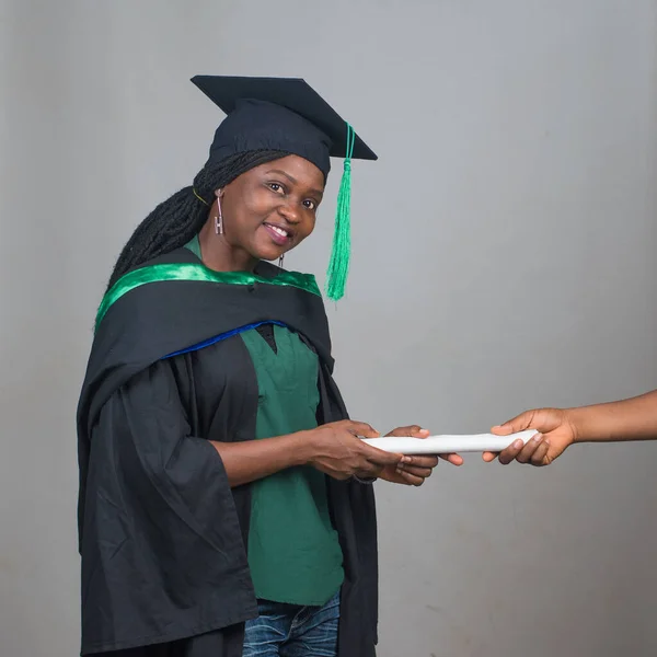 Portrait of an excited African female student or graduand from Nigeria, wearing graduation gown and cap while posing for the camera and celebrating success in education