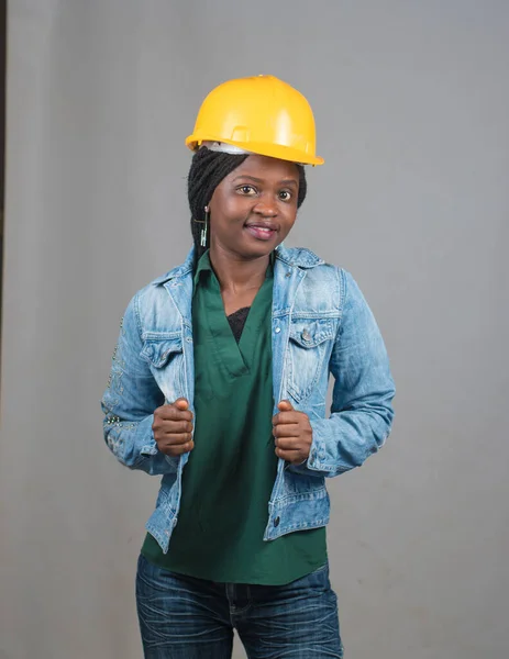 Portrait of a happy African lady or woman from Nigeria with blue jacket and yellow safety helmet representing industrial professionals like construction specialist, builders, architect and engineer
