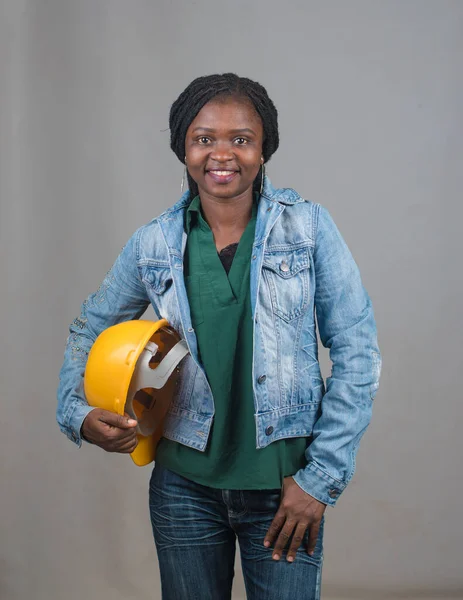 Portrait of a happy African lady or woman from Nigeria with blue jacket and yellow safety helmet representing industrial professionals like construction specialist, builders, architect and engineer