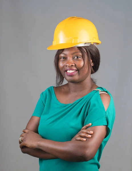 Portrait of a happy African lady or woman from Nigeria with yellow safety helmet representing industrial professionals like construction specialist, builders, architect and engineer