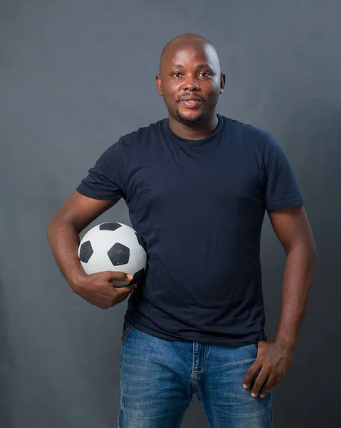 A studio portrait of a happy African man or guy holding a black and white football to his body while looking at the camera