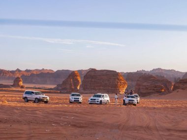 Arabalar gün batımında Arap Çölü 'nde, Suudi Arabistan' da Fil Kayası yakınlarında off-road yapıyor.