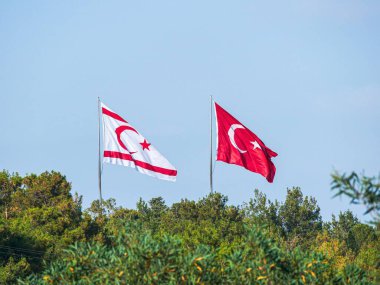 Girne, KKTC yakınlarında güneşli bir öğleden sonra büyük Türk ve Kuzey Kıbrıs bayrakları yan yana dalgalanıyor