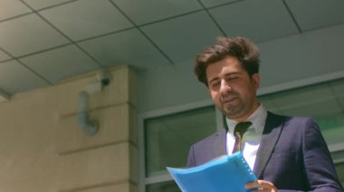 Başarılı bir iş adamının portresi şık bir takım elbise giyiyor. Elinde ofis binalarının yanında dokümanlar var..