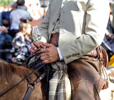 Rider on horseback dressed in traditional costume and holding glass of fino sherry (manzanilla sherry) at the April Fair (Feria de Abril), Seville Fair (Feria de Sevilla), Andalusia, Spain. Travel and tourism concepts clipart