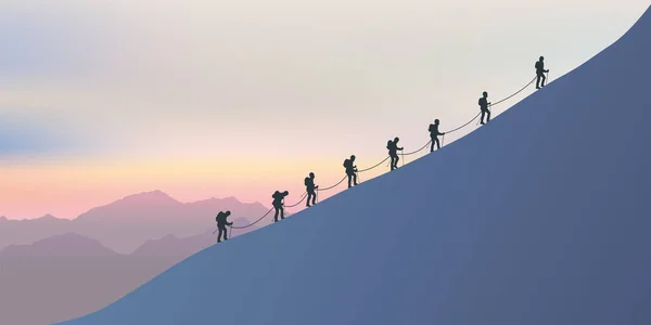 A roster of experienced alpinists climb the snowy slopes of a mountain to reach the summit. On the horizon the sun sets on the fairy landscape.