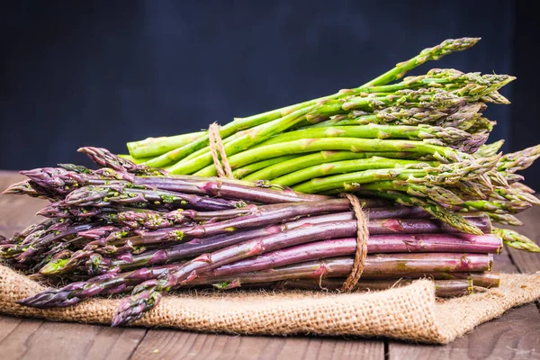Asparagus bunch green and violet on wooden background.