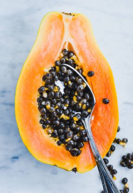 Yarım kesilmiş papaya mermer arka planda kaşık ile. Tropik yaz atmosferi, taze kesilmiş papaya..