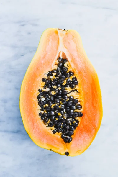 Papaya fruit open with seeds on marble background.