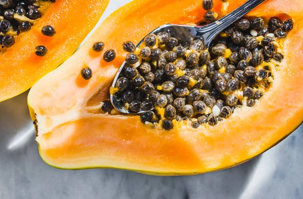 Half cut papaya on marble background with spoon. Tropical summery vibes, fresh cut papaya.