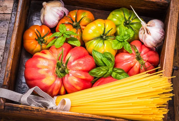 Fresh tomatoes and spaghetti pasta ,basil ingredients on wooden background.Traditional Italian ingredients for cooking pasta with tomatoes sauce.