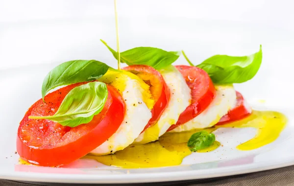 Mozzarella and tomatoes, basil salad.Italian caprese salad in white plate close up copy space background.