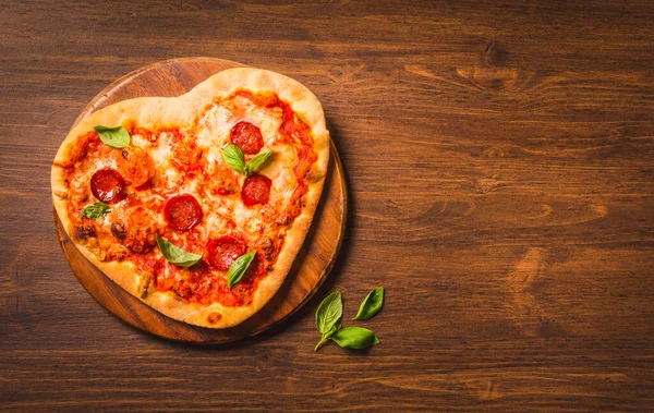 Pizza heart shaped pizza on wooden background copy space. Delicious Italian pizza delivery concept menu.