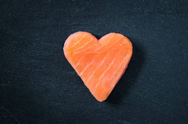 Salmon copy space on black slate background, healthy eating omega 3 concept. Heart shaped salmon steak.