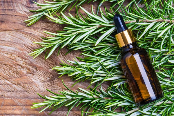 Rosemary oil bottle on wooden background copy space. Essential oil, aromatherapy natural remedies.
