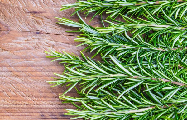 Fresh rosemary herb on wooden background top view, copy space.
