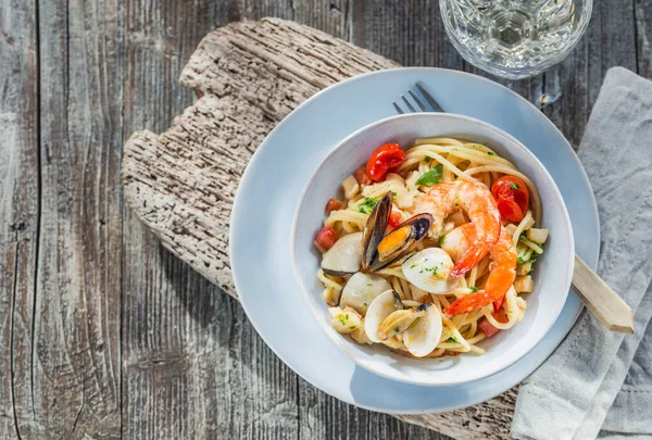 Pasta with seafood shrimps, clams, mussels on wooden summer table typical Italian seafood spaghetti recipe.