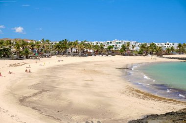 Costa Teguise Plajı, Lanzarote, mavi gökyüzünün altında oteller ve palmiye ağaçları. İspanya 'daki Kanarya Adalarına Seyahat.
