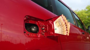 A bundle of fifty euro bills at a car's open fuel tank, slow motion shot, symbol for the rising fuel price.