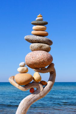 Mavi gökyüzü ve deniz zemininde, ahşap bir çıkıntıda çok renkli dengeli taşlar. Uyum, denge ve meditasyon kavramı