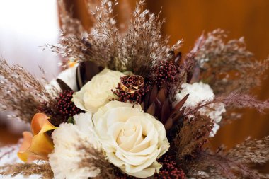 Gelin için altın alyanslı düğün buketi beyaz sarı turuncu turuncu farklı renklerden bir hediye ve yeni evlilerin düğününün bir özelliği olarak şenlikli bir ruh hali için kapalı alanda kuru otlar.