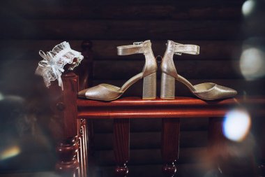 Sanat eserleri. Düğün aksesuarları, fildişi renkli kadın şenlik ayakkabıları, altın alyansları, kahverengi korkuluklarda beyaz bir jartiyer, karanlık bir odada bir dairenin içinde..