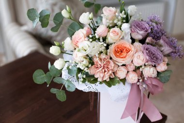 Pastel renkli güllerden yapılmış, pembe kurdelelerle süslenmiş süslü bir çiçek buketi, gün boyunca parlak bir otel odasındaki bir masanın üzerinde duruyor..