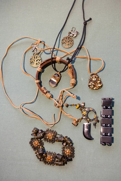 Boho tarzında bir mücevher kompozisyonu. Bilezikler, boynunda kolyeler, gri arka planda sarı renkte küpeler. Etnik, vahşi motifler, çingeneler.
