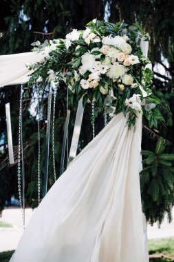 Gelin ve damat için şenlikli düğün kemeri, canlı taze çiçekler, cam kolyeler ve beyaz kumaşlarla süslenmiş, ağaçların arka planında, sokakta, evlilik töreni için..
