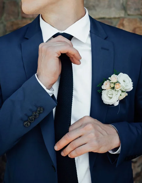 Mavi takım elbiseli, siyah kravatlı, beyaz gömlekli şık bir damat kravatını düzeltir ve yana bakar. Düğün günü için sabah hazırlıkları.
