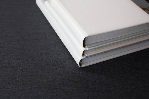 Три белые стильные фотокниги с кожаными чехлами разных размеров лежат на темной серой поверхности в комнате.