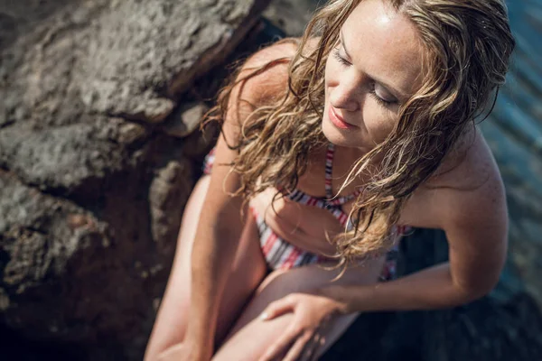 Blonde Girl Long Hair Striped Swimsuit Sits Rocks Ocean Bright — Stock Photo, Image