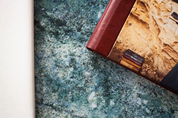 A composition of a two stylish photo books with a leather cover in white, burgundy and brown, with hardcover, lie on a textured blue stone tabletop.