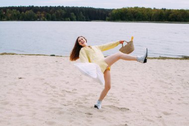 Sarı kıvırcık saçlı bir kız, elinde sepet ve yastıkla sarı bir gömlek giymiş nehir kıyısındaki kumsalda koşup gülüyor. Sepette bir şişe şampanya var..