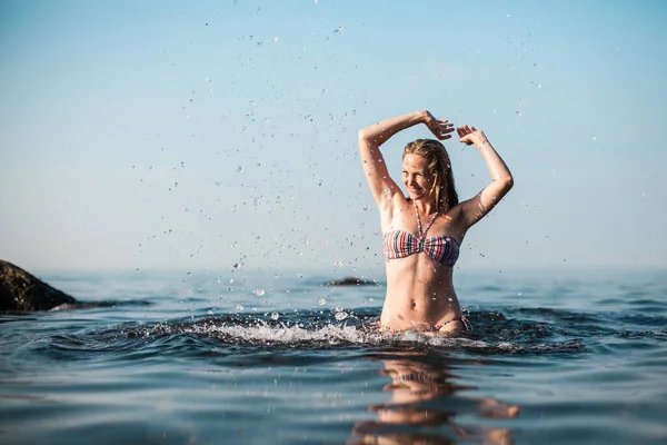 在一个阳光灿烂的日子里 一个金发碧眼 身穿条纹泳衣的女孩在海里洗澡 — 图库照片