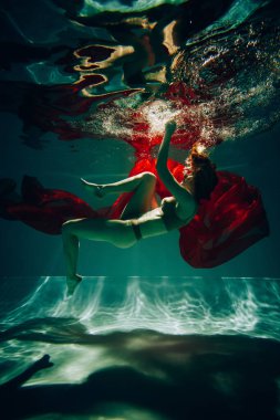 Sanat eserleri. Havuzda güzel röfleli kırmızı kumaşla iç çamaşırlı bir kızın sualtı çekimi..