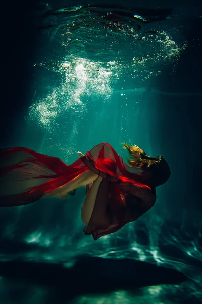 艺术品 水底拍摄的一个体育女孩与红色的材料在游泳池与美丽的亮点 — 图库照片