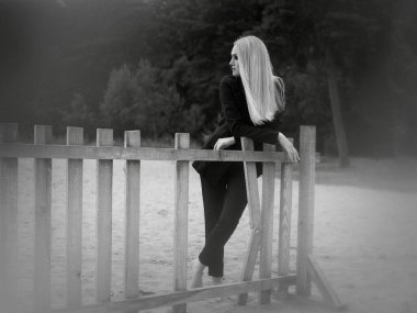 Sanat eserleri. Siyah ve beyaz bir fotoğraf, kumsalda duran, kırık ahşap bir çite dayanan sarı saçlı güzel bir kızın..