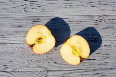 Olgun kırmızı elmanın iki yarısı gün boyunca açık ahşap bir zeminde yatar..