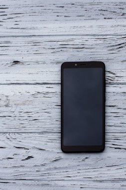 Görüntü olmayan siyah bir cep telefonu açık ahşap desenli bir yüzeyde yatıyor..