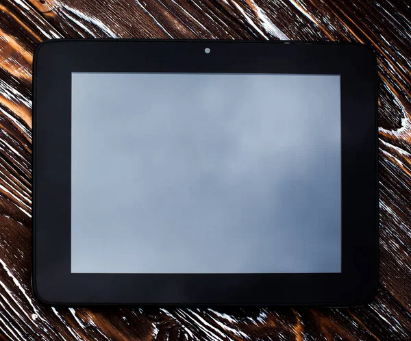 A black tablet with a blank display without an image lies on a dark wooden textured surface