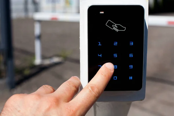 The client touches the card reader for access cards to enter the parking lot with his finger, in the background there is a white barrier with red stripes blocking the entrance.